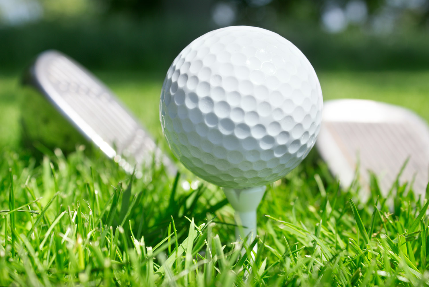 Golfball auf Tee und Schläger in grünem Gras